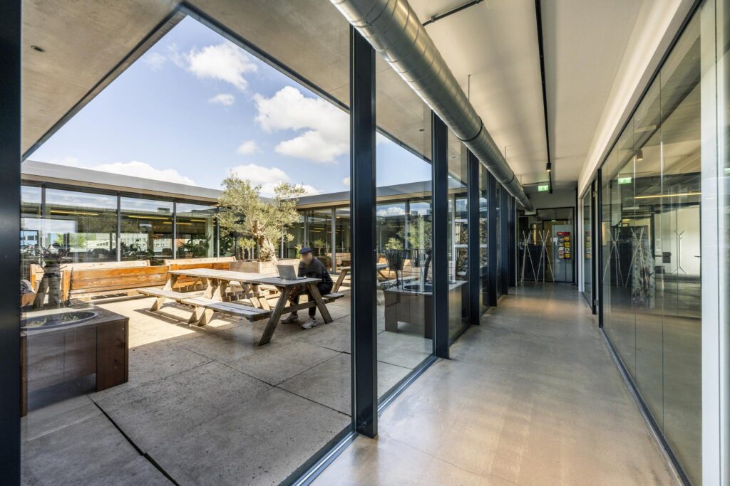 Modern office courtyard with wooden picnic tables and glass corridor at Johan van Hasseltweg.
